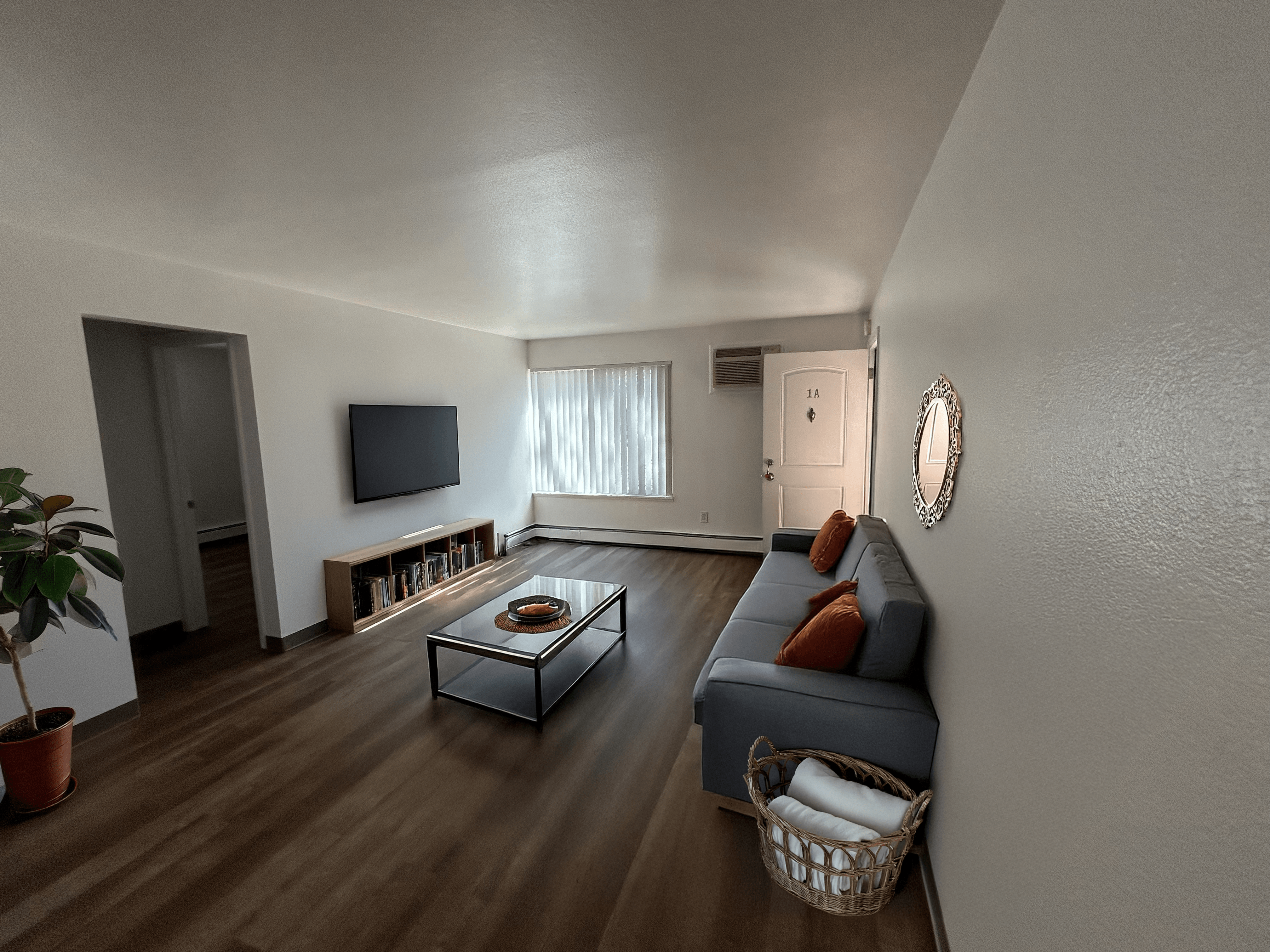A living room with a blue couch, a glass coffee table, a flat screen TV, and a potted plant.